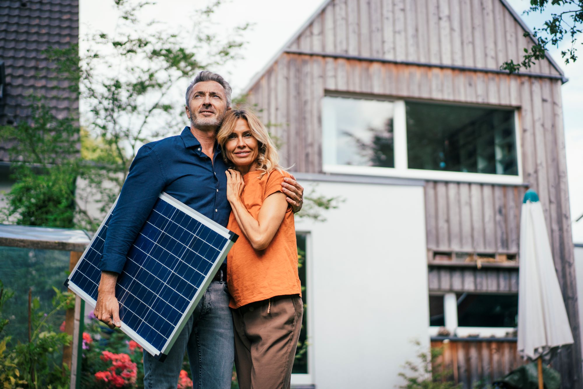 Paar steht mit Solarplatte vor Haus